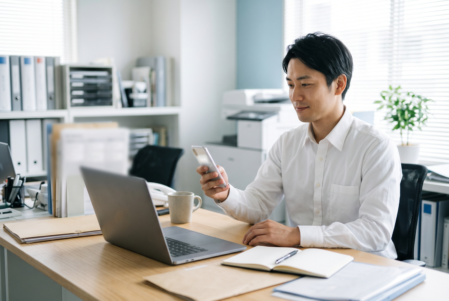 スマートフォンのお知らせを見ながら仕事を進める社員