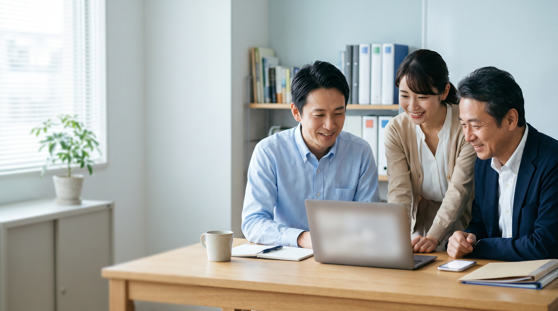 明るい事務所で、ひとつの画面を見ながら笑顔で話す3人